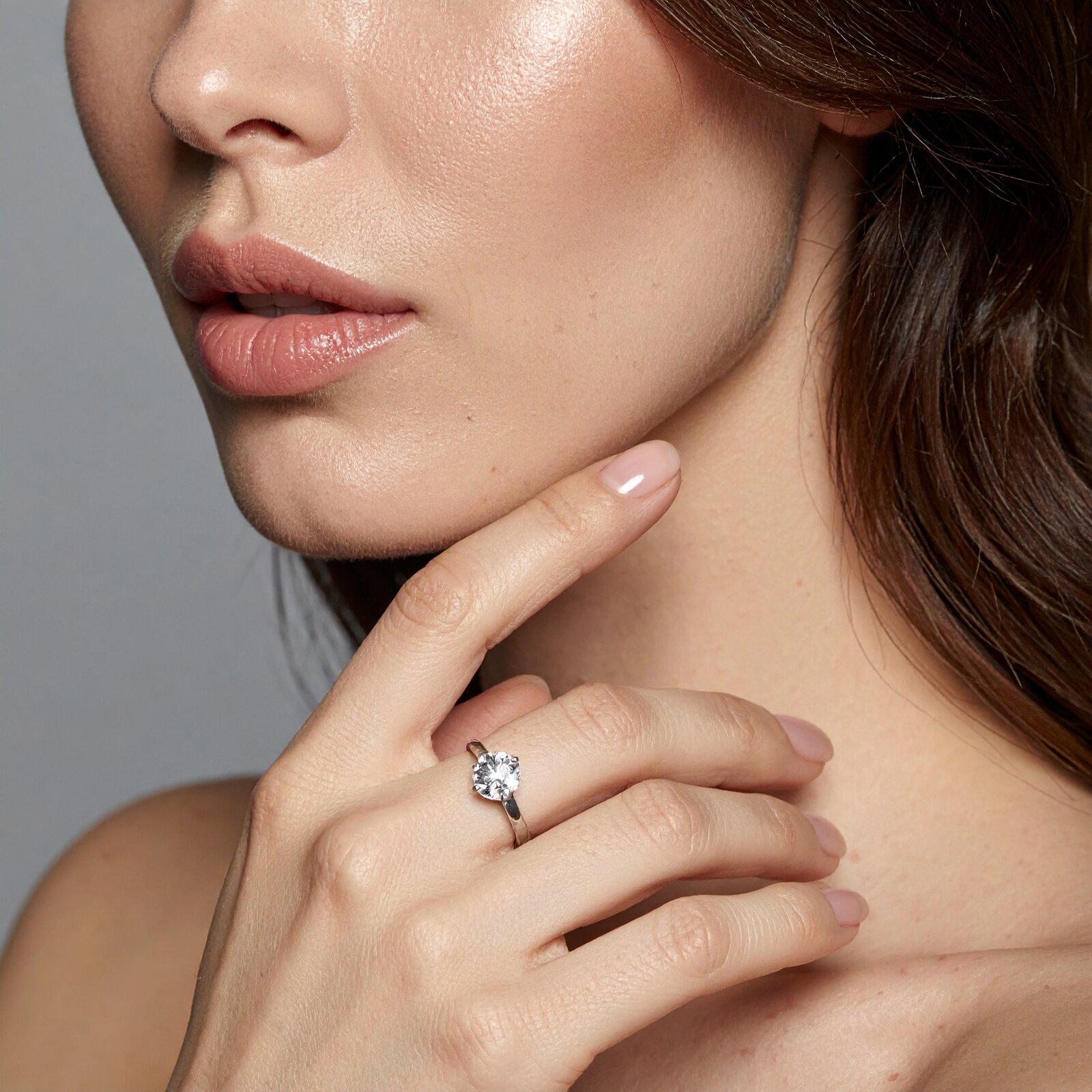 Woman wearing a 1CaratDiamond solitaire ring, hand raised to her neck in golden light